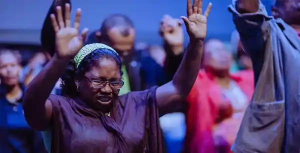 Várias pessoas com as mãos levantadas e olhos fechados orando em uma igreja. 12 Verdades Que Precisamos Saber Sobre A Oração.